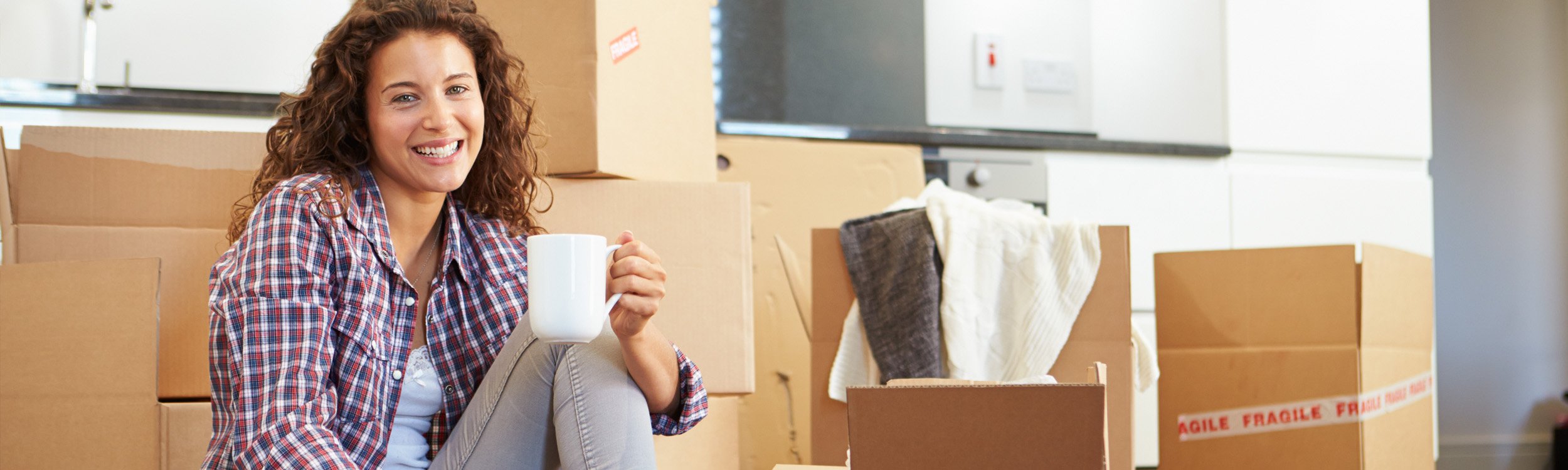 smiling girl holding coffee sitting on floor with moving boxes